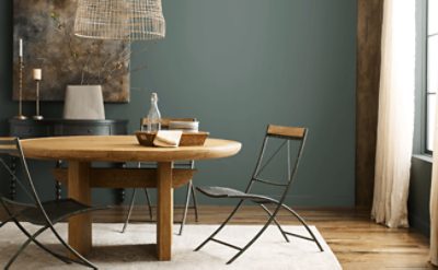 Dining room with large round wooden table, unique chairs, dark green walls with decor.