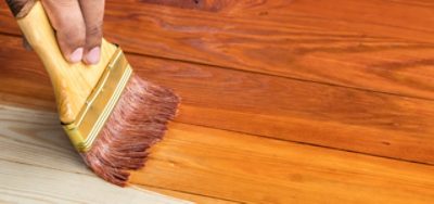 Detail shot of a person using a brush to apply wood stain onto wood, highlighting the rich finish.