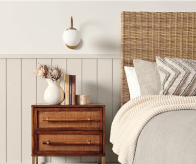 A bed with a white blanket and throw pillows and wooden mesh headboard next to a small wooden nightstand.