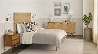 A bedroom with a bed with throw pillows, nightstand, dresser and small plant.