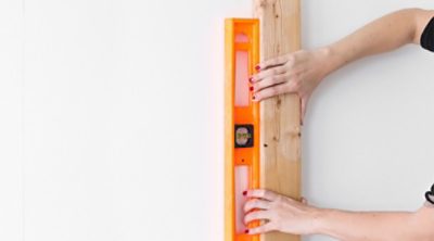 A person holding a leveler against a wooden board. 