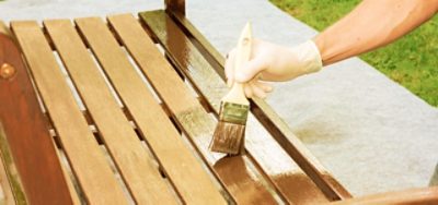 Applying stain to a wooden bench with a brush.