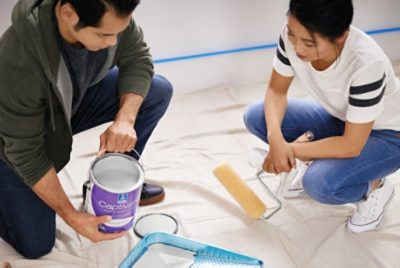 Two people getting ready to paint by filling a paint tray for their roller.