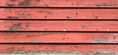 An exterior red wooden surface with paint peeling. 