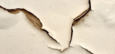 A cream colored wall with numerous paint cracks. 