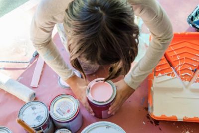 A person kneeling near paint supplies and multiple quarts of paint.