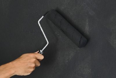 Applying chalkboard paint to a wall with a roller.