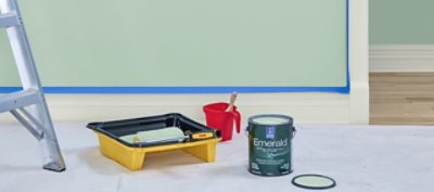 A photo of a room with paint supplies, including a ladder, one gallon of paint, and a paint tray with a paint roller.