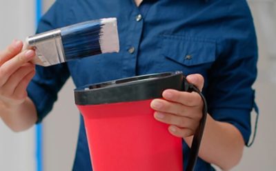 A person dipping a brush into a tub of white paint.