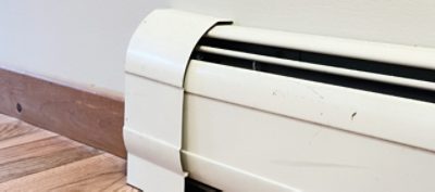 A white baseboard heater along a white wall with wood floors and baseboards.