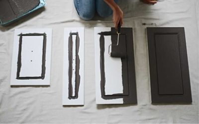 A person painting cabinet doors a dark gray.