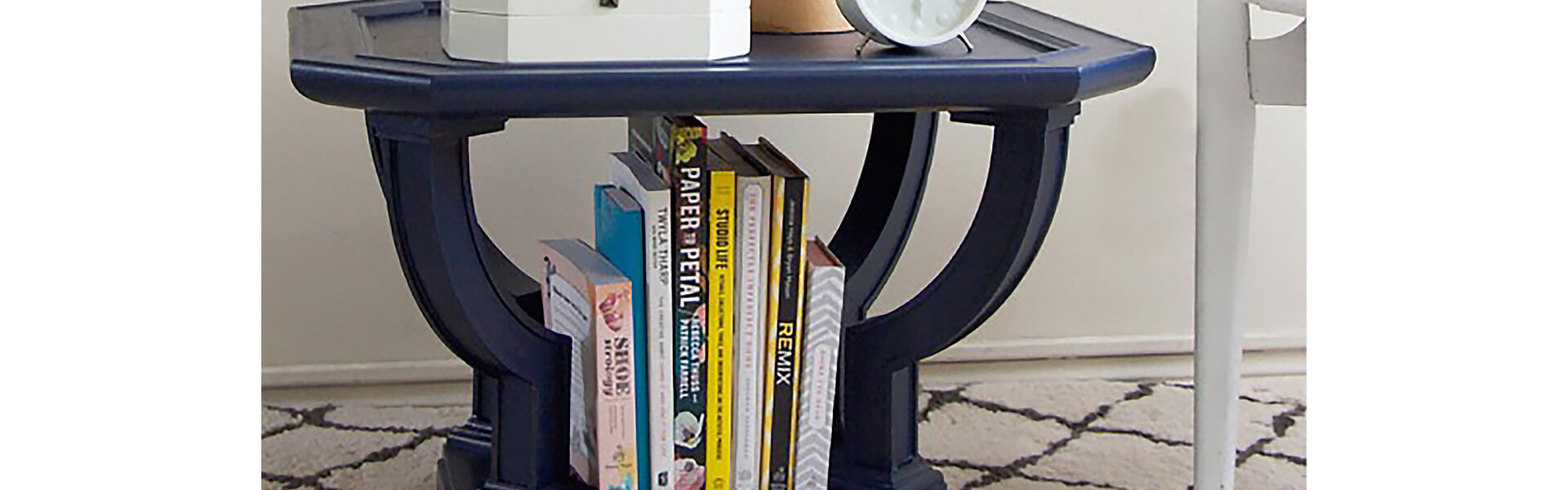 A navy blue end table with books and magazines. 
