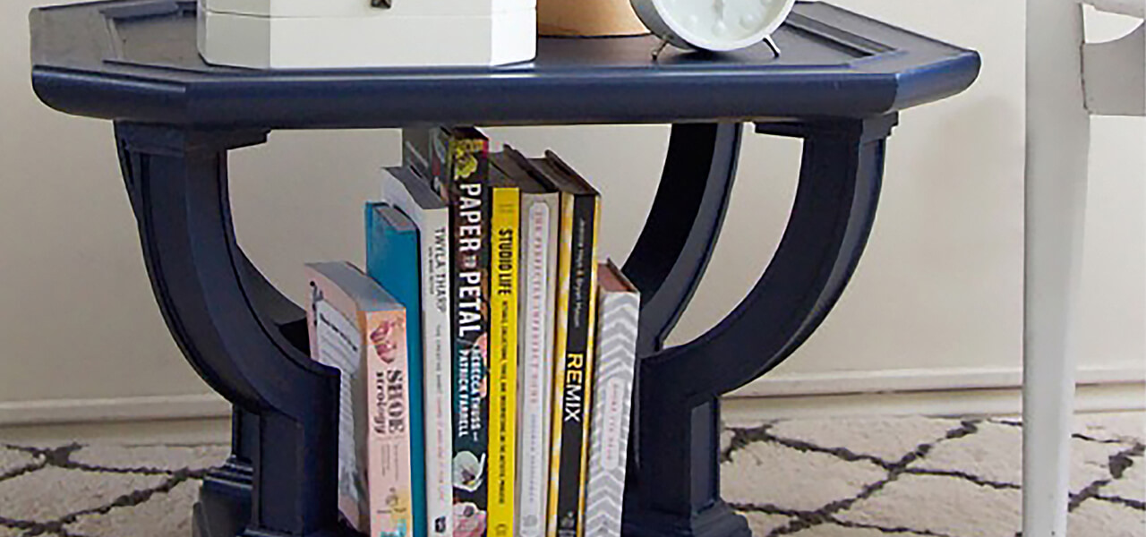 A navy blue end table with books and magazines. 