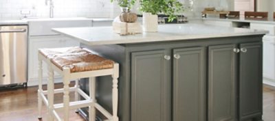 A kitchen island with white granite countertops and olive green cabinetry. 