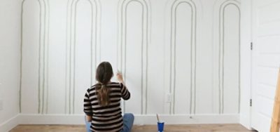 A woman painting archs on a bedroom wall. 