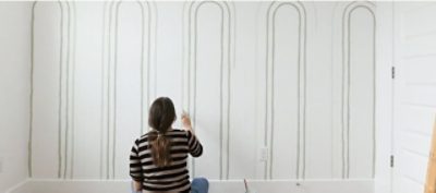 A woman painting ombre archs onto a wall. 