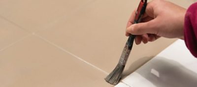 A person painting tile with a paint brush.