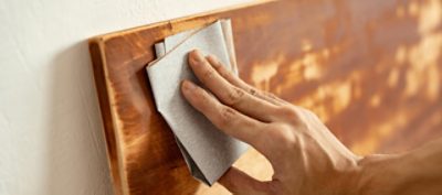 A person using sandpaper to sand a piece of stained wood.