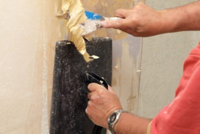 A person removing wallpaper using a steamer.