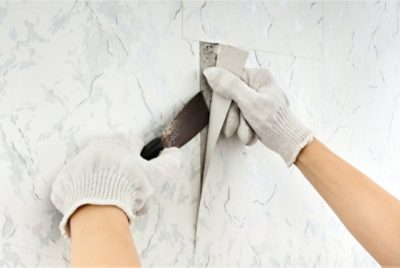 A person removing wallpaper using stripper.