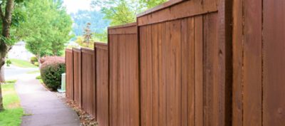 A stained wood fence next to a sidewalk.