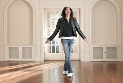 A happy person in a room with wood floors and off white walls.