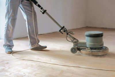 A person using an orbital sander on wood floors.