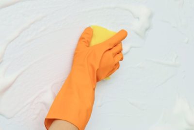 A close-up of a person's hand wearing protective gloves, scrubbing a wall with a yellow sponge.
