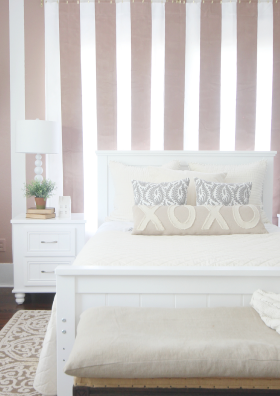 A bedroom with vertical striped wall behind a white bed by influencer Thistlewood Farms.