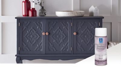 A bluish gray sideboard with a white bowl and clear and red vases on top. An aerosol can of white pigmented Shellac Primer.