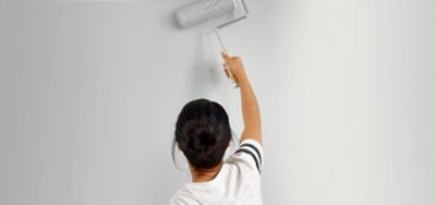 A woman painting a white wall with a roller. 