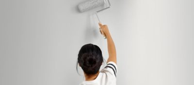 A woman painting a wall white with a paint roller. 