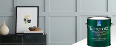 A light gray batten wall with wooden drawers in front with a picture resting on top. Featured product Emerald Interior Acrylic Latex.