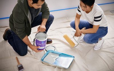 Two people painting a bedroom with white paint.