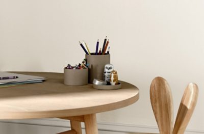 A stained wood child's table with crayons, colored pencils and small toys on top.