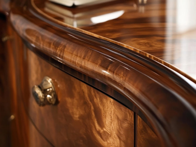 Close-up of a polished wooden cabinet with brass handles and curved edges.
