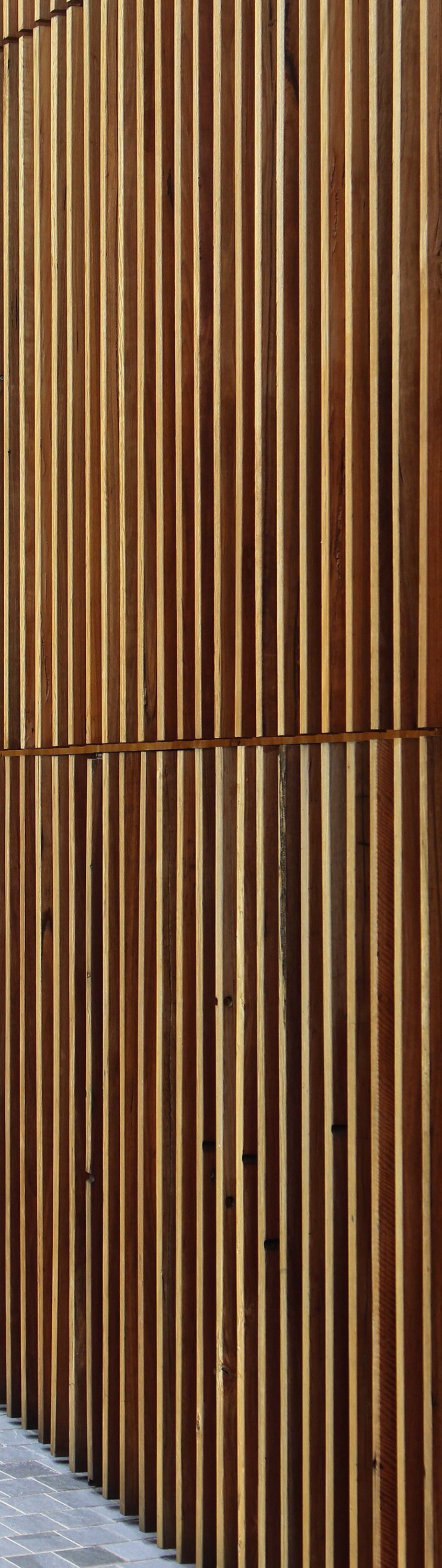 Building facade with vertical wooden cladding made of narrow natural-finish slats, and a door integrated into the design.