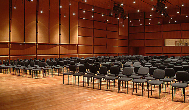 Empty auditorium with black chairs, wooden floors, and ceiling spotlights.