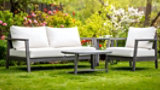 Outdoor sofa with white cushions and grey wooden frame, set in a lush garden.
