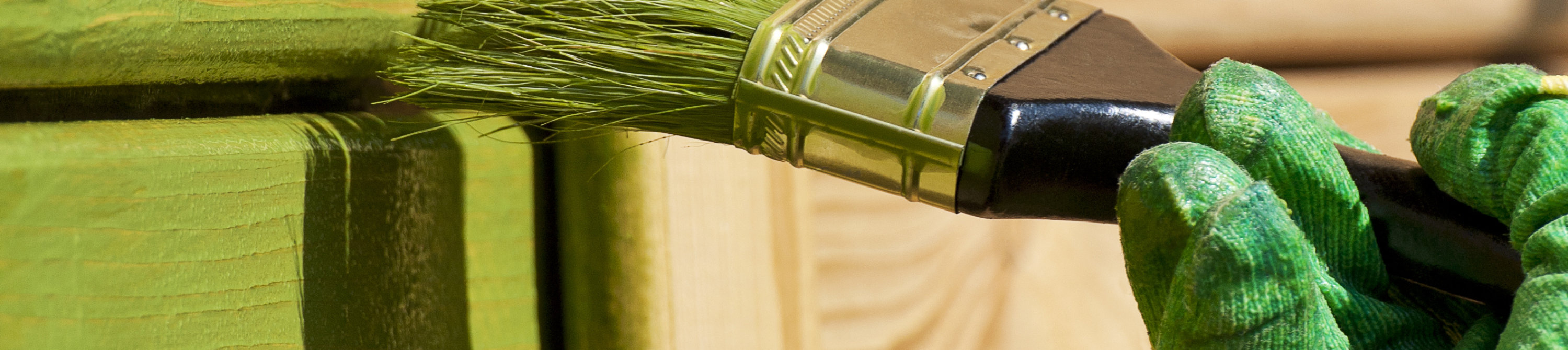 Paintbrush applying green Sayerlack wood coating to exterior wooden panels, ensuring even coverage and long-lasting protection