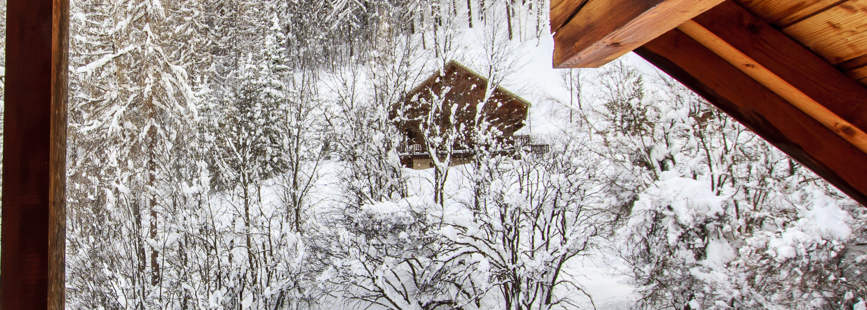 View from underneath a wooden attic with exposed beams and planks, set against a snowy outdoor landscape.
