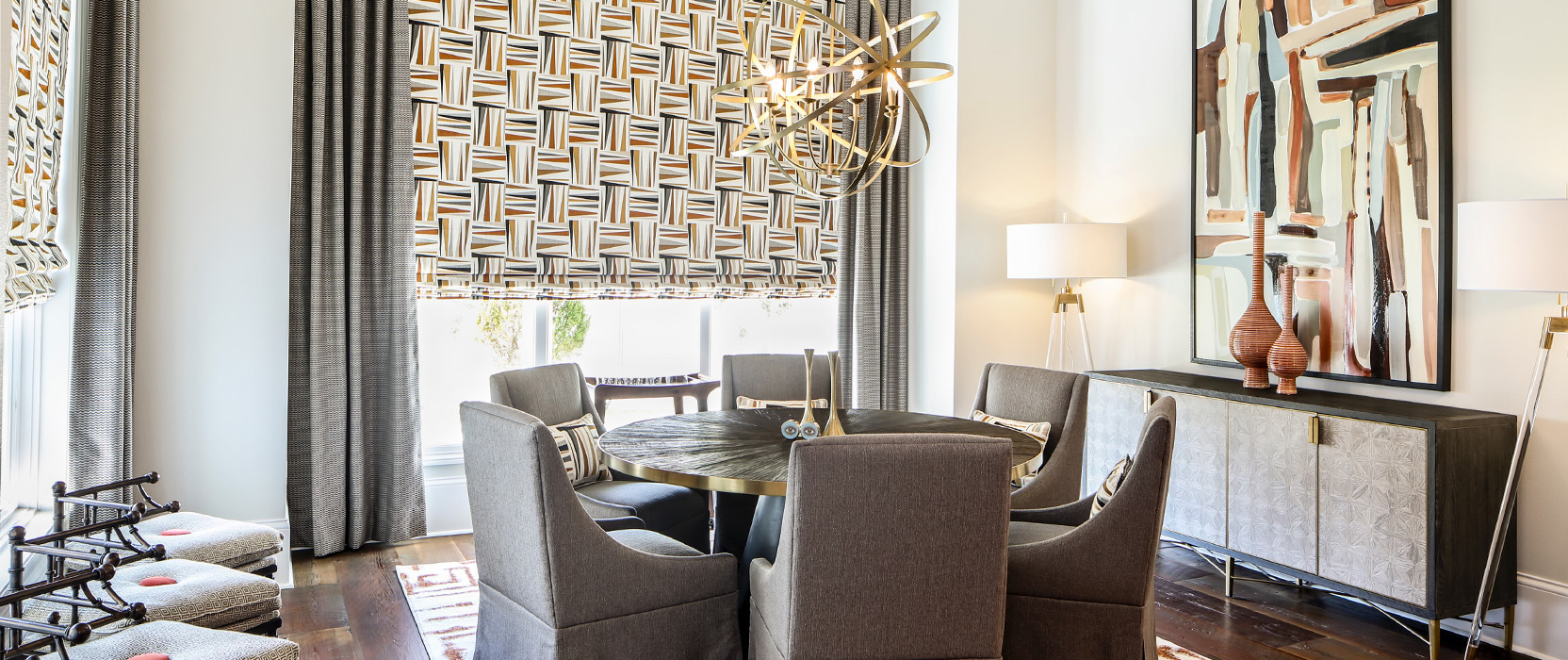 Boldly designed dining room with round table encircled by six upholstered dining chairs, patterned window coverings and modern gold orb chandelier.