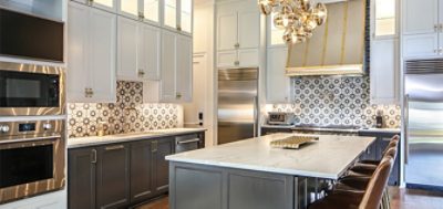 Kitchen with high ceilings, tiled backsplash, two-toned cabinets, metallic hardware and large marble-topped island.