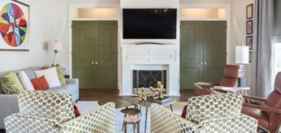 Living area with white painted fireplace and mounted flatscreen flanked by olive-colored inlaid built-ins with comfortable seating, lots of throw pillows, and organic-shape nesting coffee table.