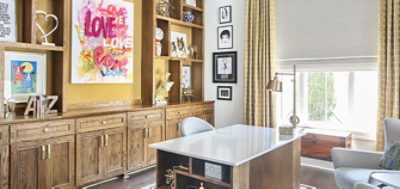 Home office area with clean white desktop in front of wood built-in bookshelves and colorful art and accessories arranged throughout.
