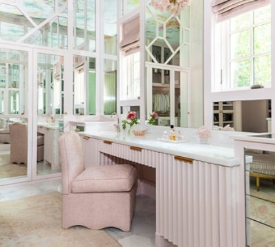 Pastel pink fluted vanity area with pink upholstered chair and high floor-to-ceiling mirrors..