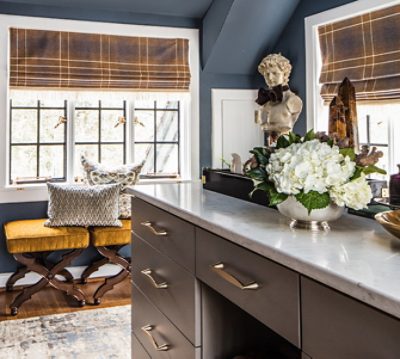 Men's dressing room with dark gray walls, paned windows, mustard stools and decorated island.