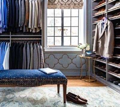 Men's dressing room full of neatly displayed suits and dress shoes, elegant blue bench in foreground.