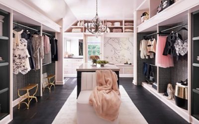 Large sunlit walk-in closet with pastel pink walls, clothing racks, elegant chandelier, and mural of a branch on one wall.