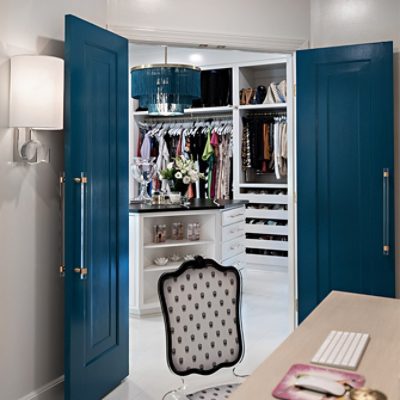 View from desk showing teal double doors with clear acrylic handles open to a large walk in closet beyond.